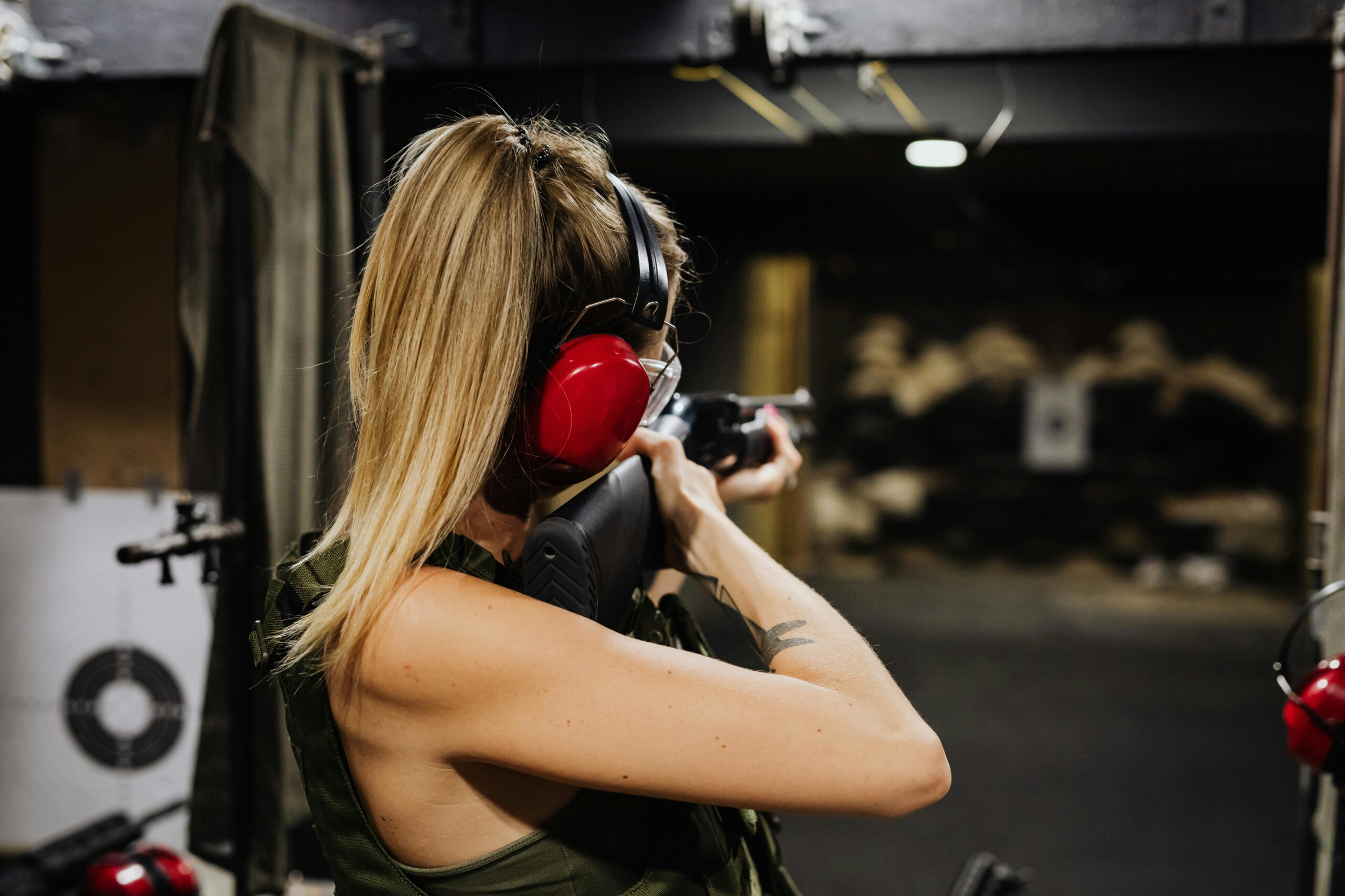 A woman aiming a rifle at a target in an indoor shooting range.